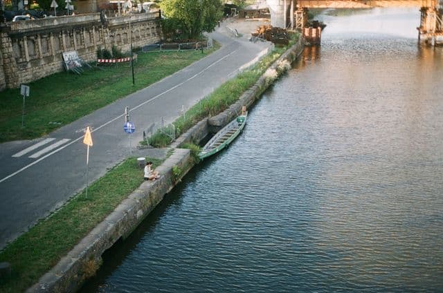 Aerial shot of riverfront in Kraków, Poland, featuring a lone boat and serene pathways.