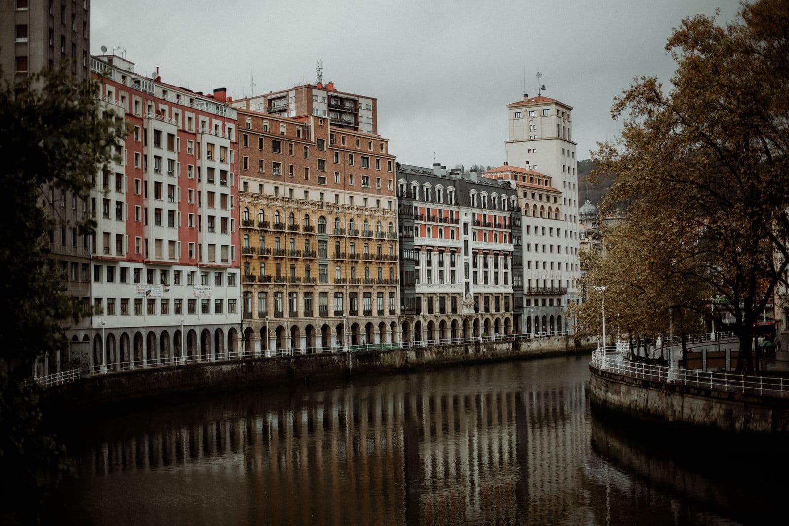 Classic 19th-century facade architecture and riverside reflections dividing Abando and Casco Viejo in Bilbao