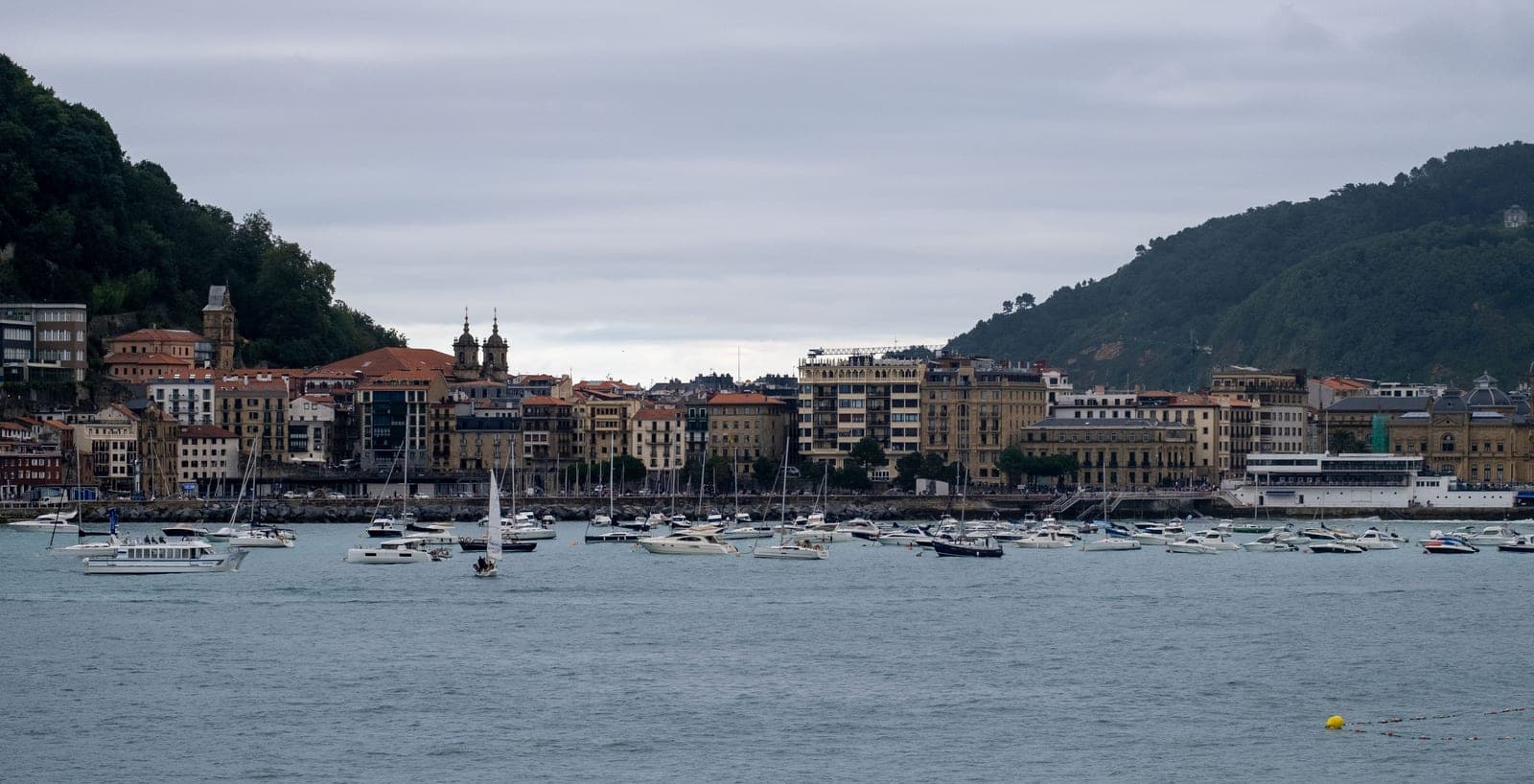 Boats anchored in the picturesque harbor of San Sebastián with a backdrop of historic buildings.