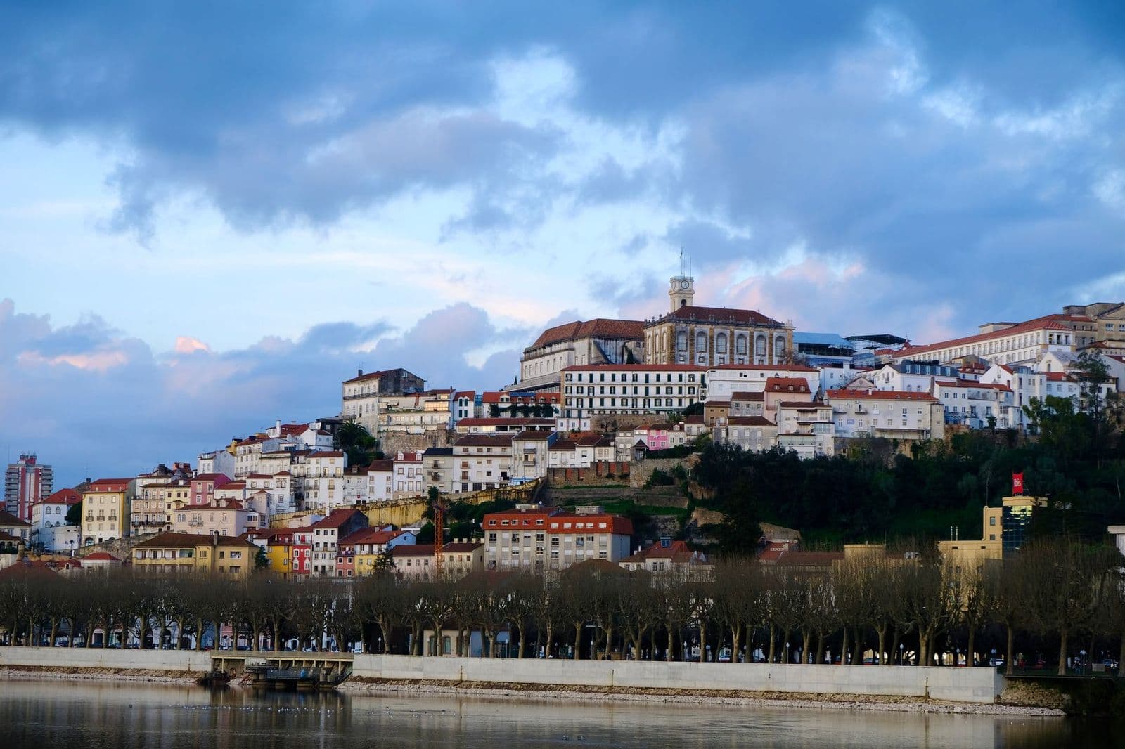 Beautiful view of Coimbra's historic architecture along the river under a vibrant sky.